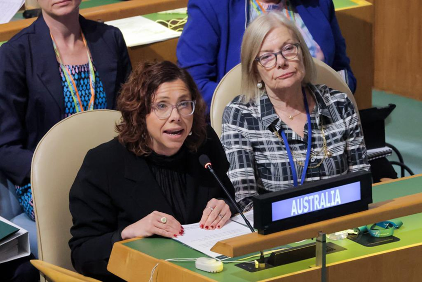 Two woman seated behind a panel desk with a sign that says "Australia". One is speaking into a microphone attached to the desk.